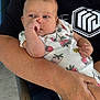Rhilley is registered to the contest to win money with this photo: baby, infant, child, person, holding, arm, clothing, onesie, pattern, strawberry, face, hand, nose_picking, seated, adult, black_shirt, logo, skin, portrait, indoor