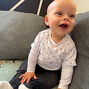 Këyden participe au concours pour gagner de l'argent avec cette photo : baby, child, smiling, couch, blanket, white_shirt, dark_pants, socks, happy, indoor, person, seated, cozy, face, head, hand, footwear, home, comfort, cute