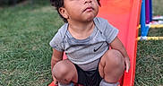Robert is registered to the contest to win money with this photo: black_shorts, child, clothing, curious, curly_hair, cute, daylight, fisher_price, grass, gray_shirt, outdoor, person, play, playground, sitting, slide, socks, toddler, toy, young_child