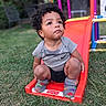 Robert is registered to the contest to win money with this photo: toddler, child, slide, playground, grass, curly_hair, socks, clothing, outdoor, toy, fisher_price, gray_shirt, black_shorts, sitting, person, cute, young_child, daylight, play, curious