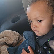 J'Marcus is registered to the contest to win money with this photo: baby, blanket, car_seat, child, closeup, clothing, comfort, curly_hair, expression, fabrics, face, hand, indoors, person, portrait, seatbelt, serious, sitting, toddler, young_child