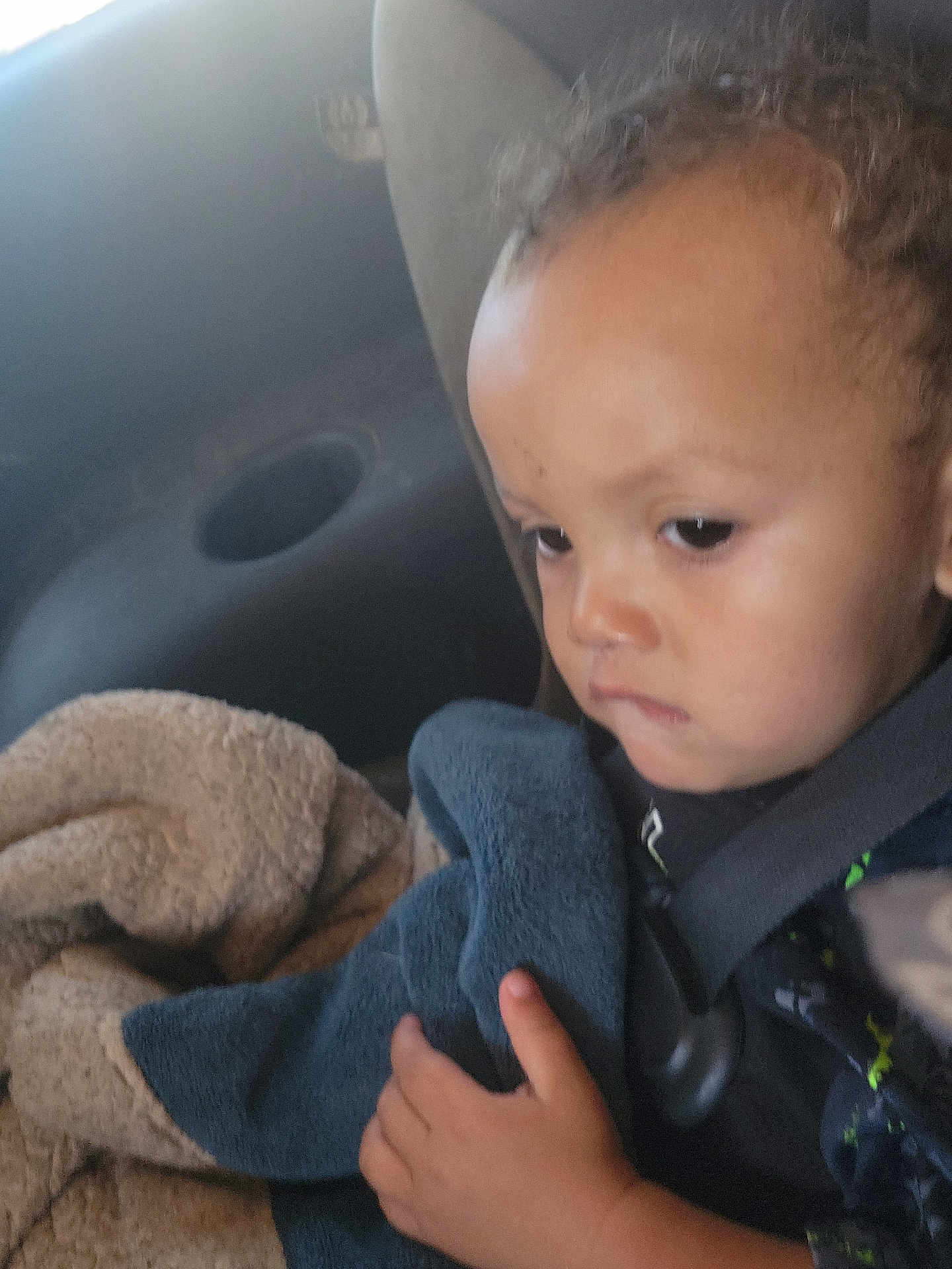 J'Marcus is registered to the contest to win money with this photo: baby, blanket, car_seat, child, closeup, clothing, comfort, curly_hair, expression, fabrics, face, hand, indoors, person, portrait, seatbelt, serious, sitting, toddler, young_child