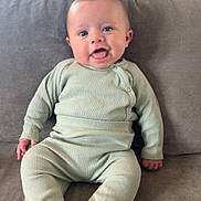 Ernie is registered to the contest to win money with this photo: baby, child, infant, pajamas, ribbed_clothing, sitting, couch, sofa, grey, smiling, happy, indoors, living_room, face, person, cute, young, comfort, home, portrait
