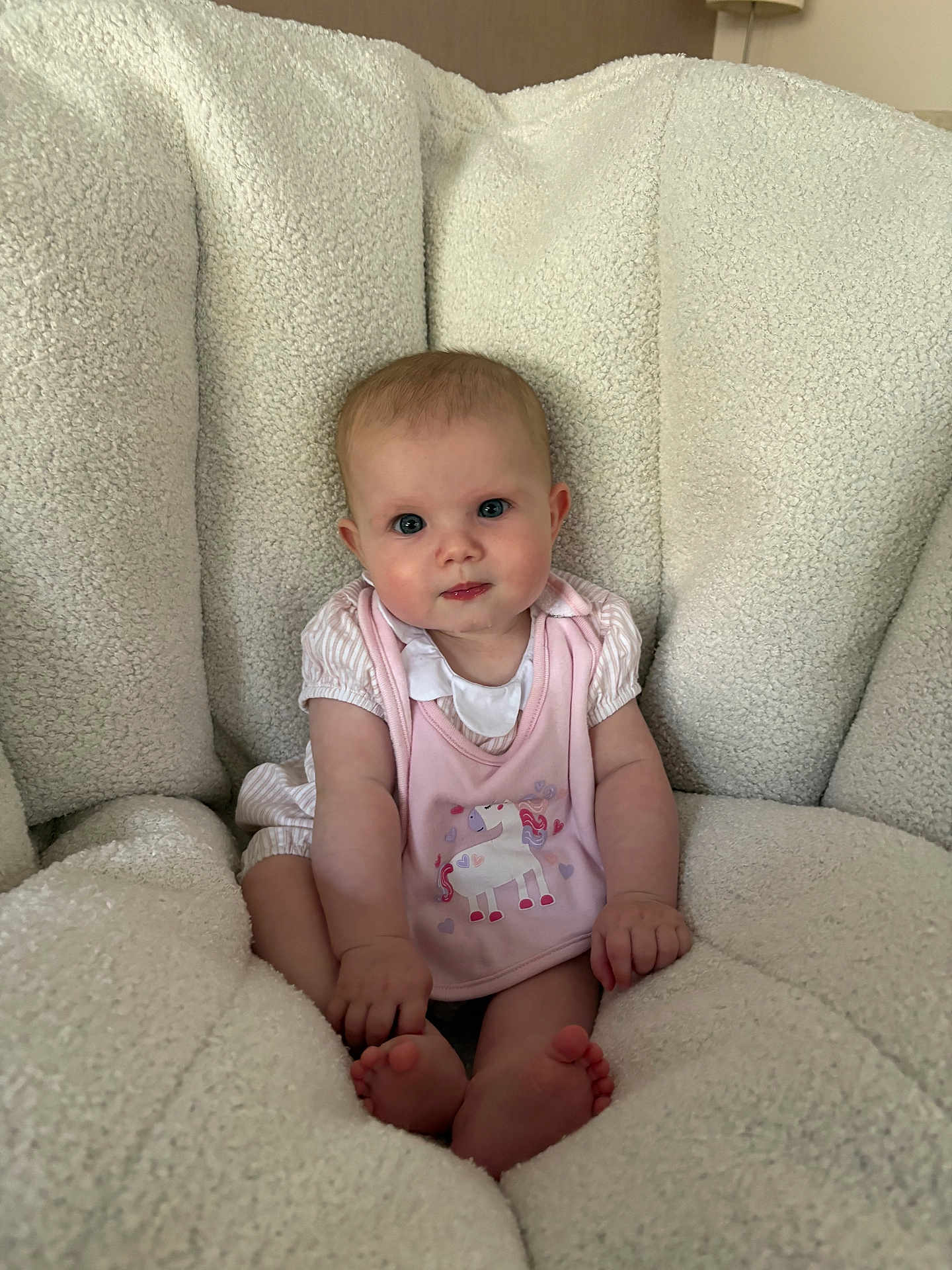 Georgia is registered to the contest to win money with this photo: baby, infant, child, pink_bib, unicorn, blue_eyes, fluffy_chair, cozy, cute, sitting, clothing, indoor, portrait, soft_texture, small_feet, curious_expression, person, young_child, comfortable, home