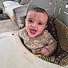 baby, blanket, child, clothing, couch, cute, expression, face, floral_pattern, furniture, happy, high_chair, home, indoor, infant, person, portrait, sitting, smile, young_child