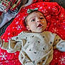 baby, infant, child, headband, bow, red_blanket, snowflake_pattern, christmas_wrapping, presents, gifts, holiday, festive, pajamas, onesie, portrait, closeup, lying_down, carpet, wide_eyed, cute