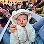 baby, infant, hooded_jacket, fluffy_coat, hand, eyes, expression, bleachers, audience, crowd, stadium, bench, people, parent, seating, candid, portrait, outdoor, evening, event