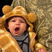 Sadie is registered to the contest to win money with this photo: baby, background_person, camouflage_pattern, close_up, cozy, cute, facial_expression, fuzzy_jacket, hand, hood, indoor, infant, knit_sweater, person, pom_pom, portrait, seat, teddy_bear, yawning, zipper