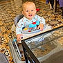baby, child, clothing, face, floor_tiles, furniture, glass, happy, head, home, household, indoor, person, play, room, sitting, smiling, table, toy, walker