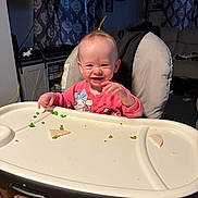 Amelia is registered to the contest to win money with this photo: baby, high_chair, food, peas, tortilla, smiling, indoor, person, child, cute, happy, face, clothing, hair, meal, table, furniture, room, curtains, home