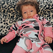 Lakelynn is registered to the contest to win money with this photo: baby, infant, child, onesie, pink_clothing, camouflage_pattern, leopard_print, cushion, furniture, indoors, portrait, face, hand, foot, hair, pouting, relaxed, person, cute, cozy