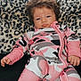 baby, infant, child, onesie, pink_clothing, camouflage_pattern, leopard_print, cushion, furniture, indoors, portrait, face, hand, foot, hair, pouting, relaxed, person, cute, cozy