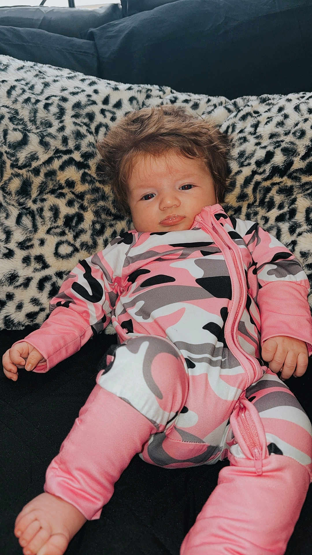 Lakelynn is registered to the contest to win money with this photo: baby, infant, child, onesie, pink_clothing, camouflage_pattern, leopard_print, cushion, furniture, indoors, portrait, face, hand, foot, hair, pouting, relaxed, person, cute, cozy