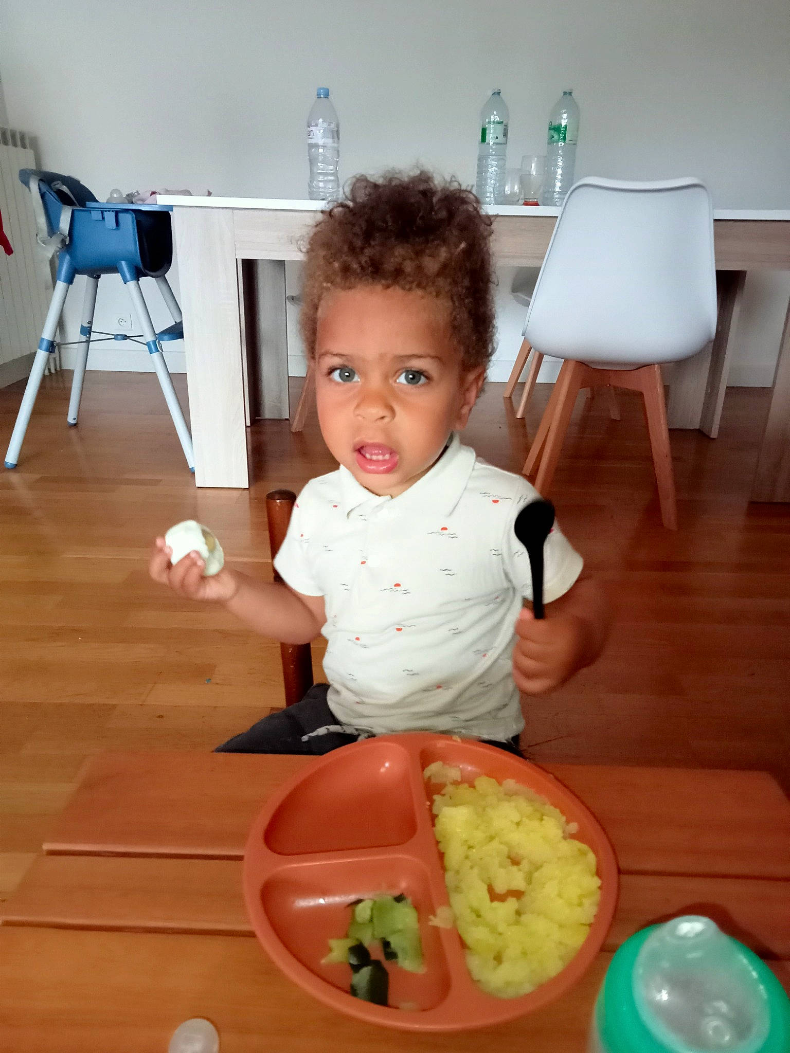Eliott participe au concours pour gagner de l'argent avec cette photo : baby, baby_toddler_clothing, blue, bottle, chair, child, comfort_food, cooking, cuisine, dish, flooring, food, hardwood, kitchen, person, room, sitting, table, tableware, toddler