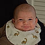 baby, infant, smile, face, bib, dinosaur_pattern, clothing, brown, texture, person, portrait, closeup, cute, child, happy, indoor, window, fabric, apparel, human
