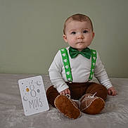 Tomy a rejoint le concours — aidez-le/la à gagner de superbes lots ! baby, child, infant, green_bow_tie, suspenders, brown_pants, soft_blanket, milestone_card, indoors, portrait, cute, sitting, curious, young_child, face, head, feet, shoes, clothing, celebration