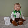 baby, child, infant, green_bow_tie, suspenders, brown_pants, soft_blanket, milestone_card, indoors, portrait, cute, sitting, curious, young_child, face, head, feet, shoes, clothing, celebration