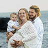 baby, child, family, parents, mother, father, smiling, portrait, outdoor, seaside, ocean, water, beach, lace_dress, white_clothing, infant, holding_child, family_photo, tattoo, photography