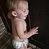 toddler, child, baby, diaper, standing, laughing, smiling, profile, face, blond_hair, bare_chest, barefoot, indoors, doorway, dark_background, wooden_floor, candid, portrait, hand, infant