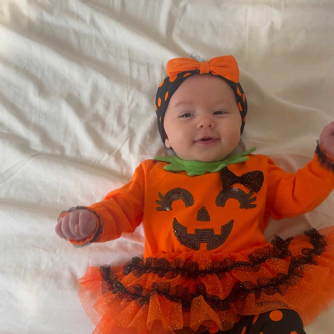 Madalynn is registered to the contest to win money with this photo: baby, child, pumpkin_costume, halloween, orange, bow, headband, smiling, lying_down, bed, blanket, tutu, ruffles, polka_dots, leggings, portrait, indoors, infant, costume, happy