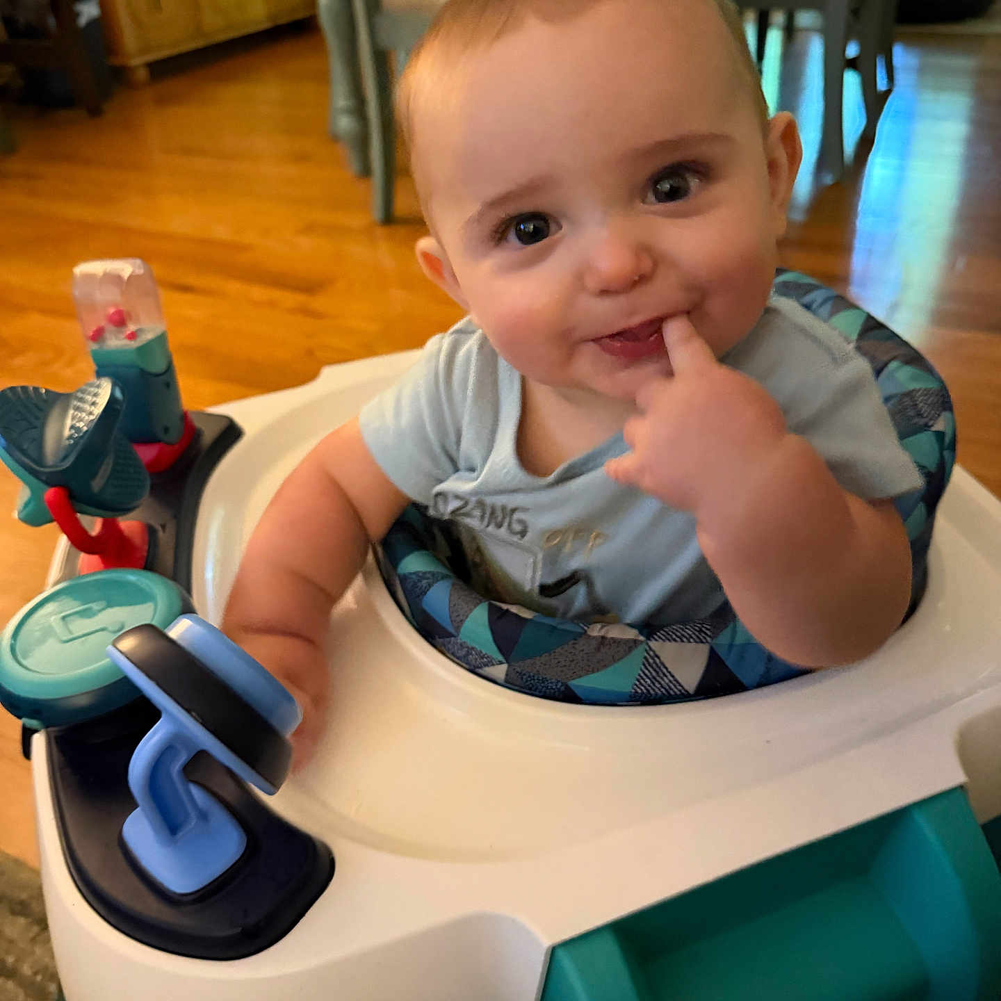Colton joined the competition — help win amazing prizes! baby, child, infant, smiling, portrait, indoors, activity_walker, baby_toy, finger, hand, blue_clothing, seated, wooden_floor, furniture, home, playtime, happy, face, photograph, family