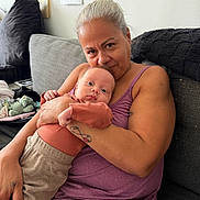 David is registered to the contest to win money with this photo: baby, infant, adult, mother, cuddling, portrait, smiling, sitting, couch, sofa, home, indoors, family, hugging, clothing, purple_shirt, blanket, stuffed_toy, tattoo, closeup