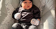 David joined the competition — help win amazing prizes! baby, baby_chair, bear_hat, black_hat, blanket, bouncer, child, cozy, cushion, dark_clothing, indoors, infant, mittens, nursery, patterned_fabric, portrait, sitting, smiling, socks, sunlight