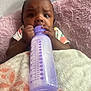 Zanaija Tate joined the competition — help win amazing prizes! baby, bottle, blanket, infant, feeding, purple, cute, hands, face, expression, lying_down, clothing, pattern, soft, indoor, child, person, cozy, bed, closeup