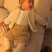 Elena a rejoint le concours — aidez-le/la à gagner de superbes lots ! baby, child, infant, headband, vest, corduroy_pants, white_shirt, couch, indoor, smiling, happy, cozy, soft_lighting, footwear, tights, person, portrait, furniture, relaxing, cute