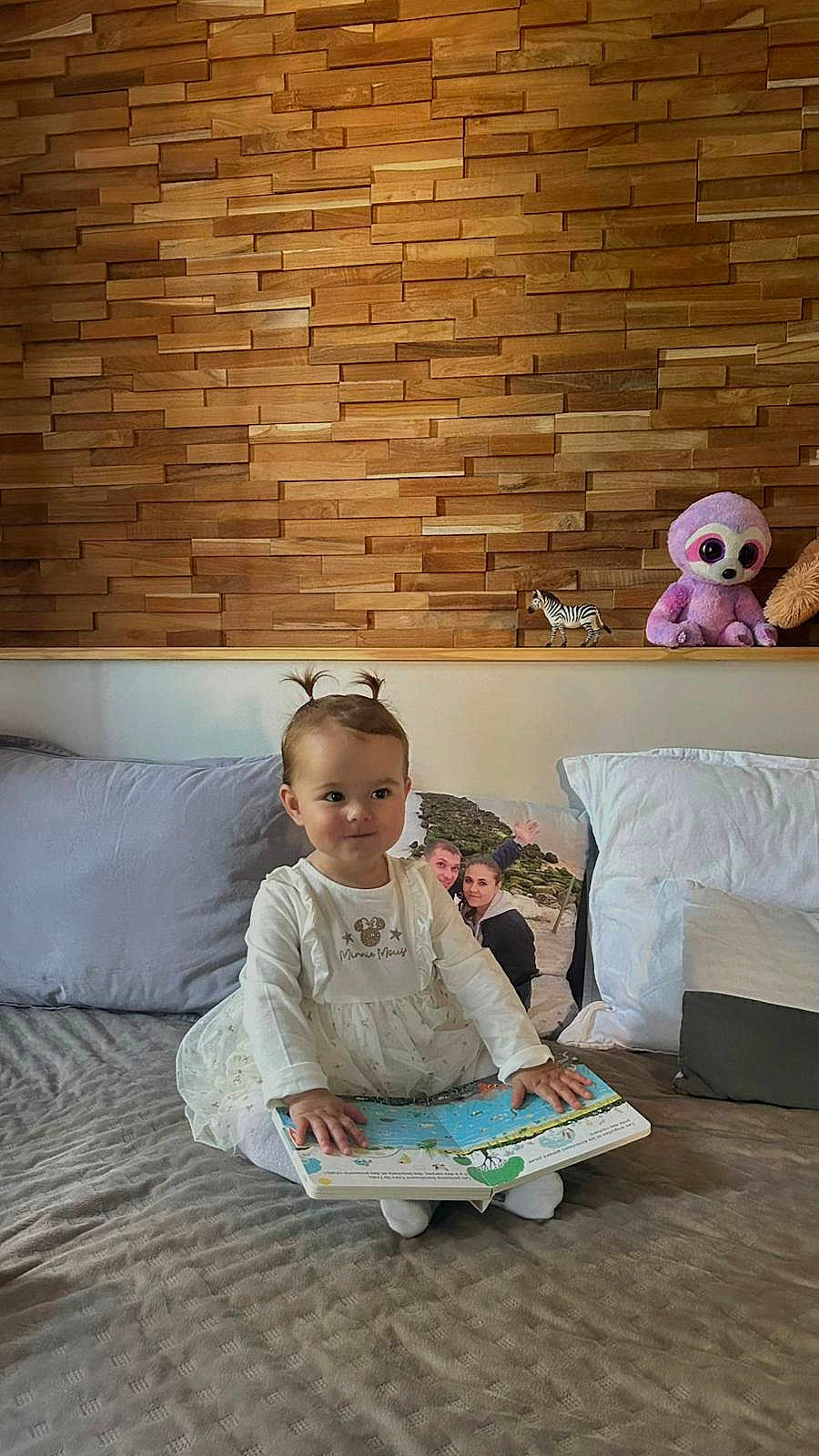 Melina a rejoint le concours — aidez-le/la à gagner de superbes lots ! toddler, child, book, bed, pigtails, stuffed_animal, toy, zebra_toy, wooden_wall, pillow, blanket, indoors, cute, smiling, white_clothing, girl, home, cozy, sitting, playful