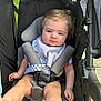 Killian joined the competition — help win amazing prizes! baby, stroller, child, infant, seatbelt, foot, curly_hair, bib, onesie, outdoor, sunlight, cute, baby_face, expression, sitting, comfort, playful, young_child, candid, portrait