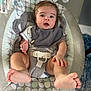 baby, infant, baby_rocker, bib, onesie, feet, face, hand, cushion, pattern, indoor, carpet, toy, seat, child, person, expression, looking, comfort, cute