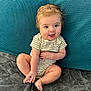 baby, child, infant, smiling, sitting, onesie, foot, hand, blanket, couch, blue_background, happy, cute, playful, indoors, skin, face, eyes, hair, young