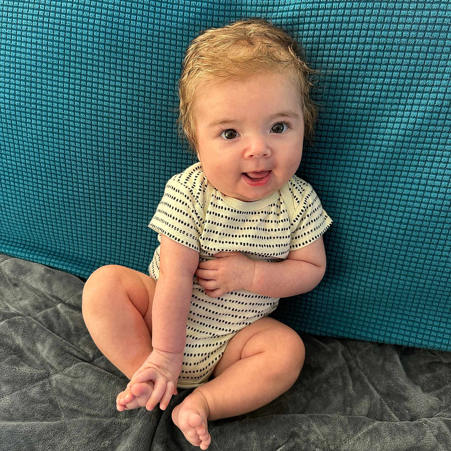 Killian joined the competition — help win amazing prizes! baby, blanket, blue_background, child, couch, cute, eyes, face, foot, hair, hand, happy, indoors, infant, onesie, playful, sitting, skin, smiling, young