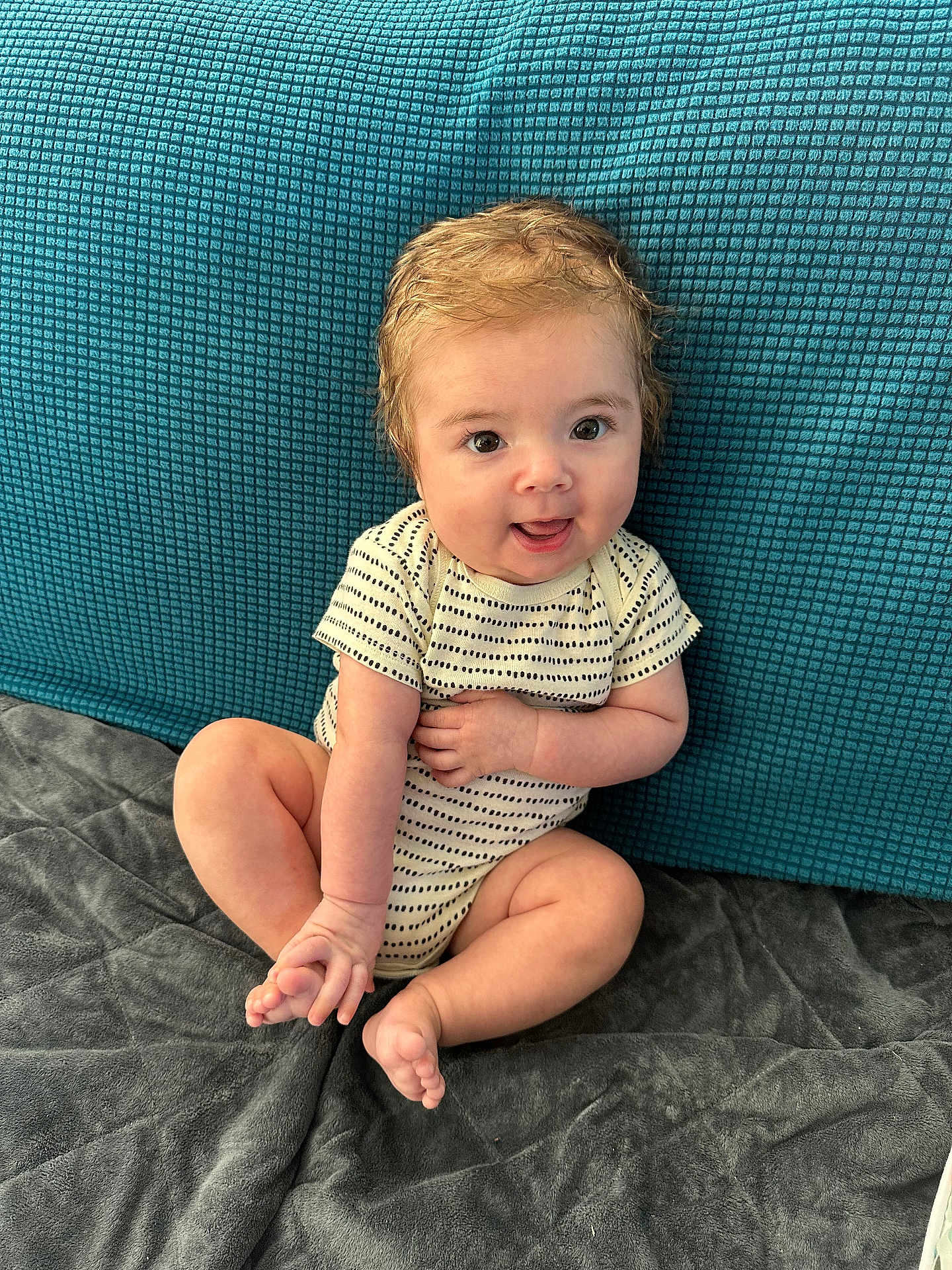 Killian joined the competition — help win amazing prizes! baby, child, infant, smiling, sitting, onesie, foot, hand, blanket, couch, blue_background, happy, cute, playful, indoors, skin, face, eyes, hair, young