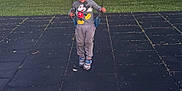 Ezequiel is registered to the contest to win money with this photo: child, swing, playground, mickey_mouse, sweatshirt, grass, rubber_tiles, shoes, young_child, outdoor, person, casual_clothing, toy, fun, leisure, daylight, standing, park, smile, curious