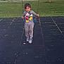 child, swing, playground, mickey_mouse, sweatshirt, grass, rubber_tiles, shoes, young_child, outdoor, person, casual_clothing, toy, fun, leisure, daylight, standing, park, smile, curious