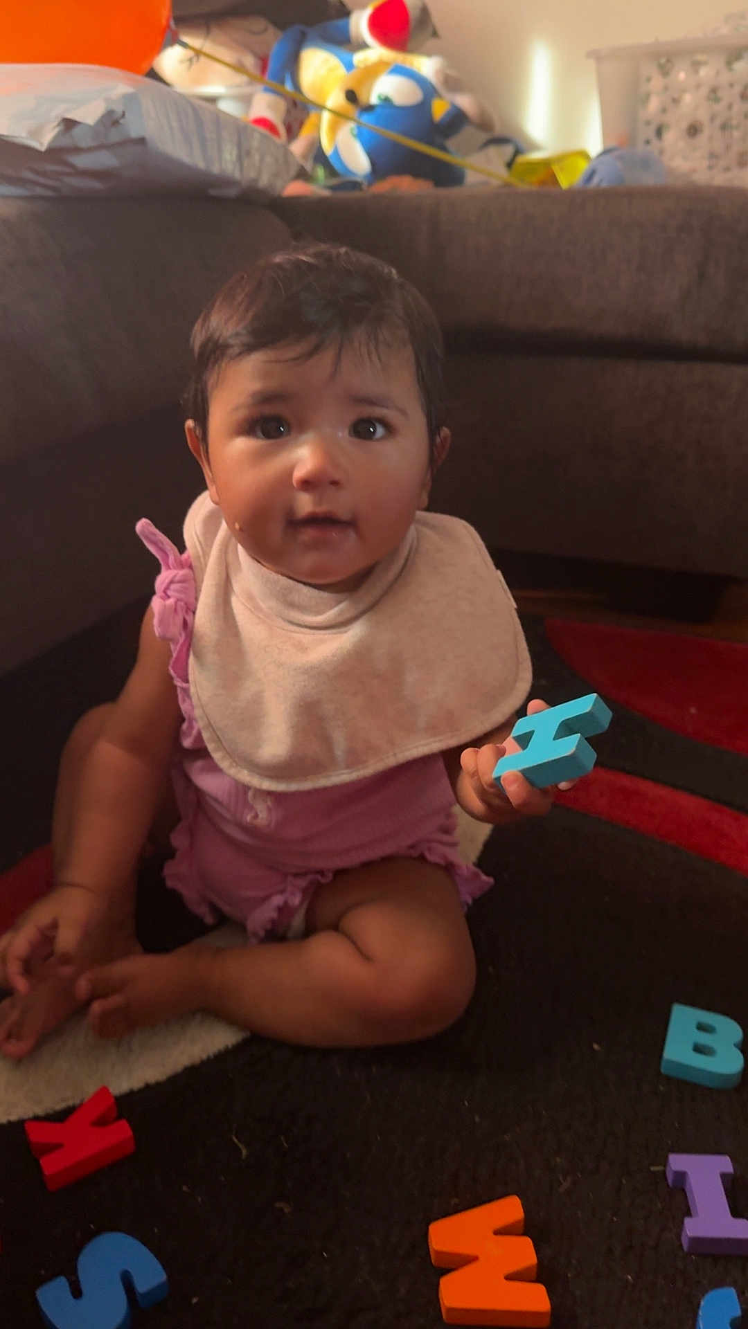 Maria joined the competition — help win amazing prizes! baby, child, indoor, carpet, alphabet_letters, toy, bib, sitting, curious, colorful, foam_letters, couch, floor, playtime, infant, young_child, pink_clothing, hand, foot, expression