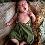 Roméo a rejoint le concours — aidez-le/la à gagner de superbes lots ! baby, infant, yawning, green_overalls, blanket, pillow, soft_texture, cozy, sleepy, cute, newborn, wooden_board, indoors, child, skin, furniture, relaxing, resting, small_person, portrait