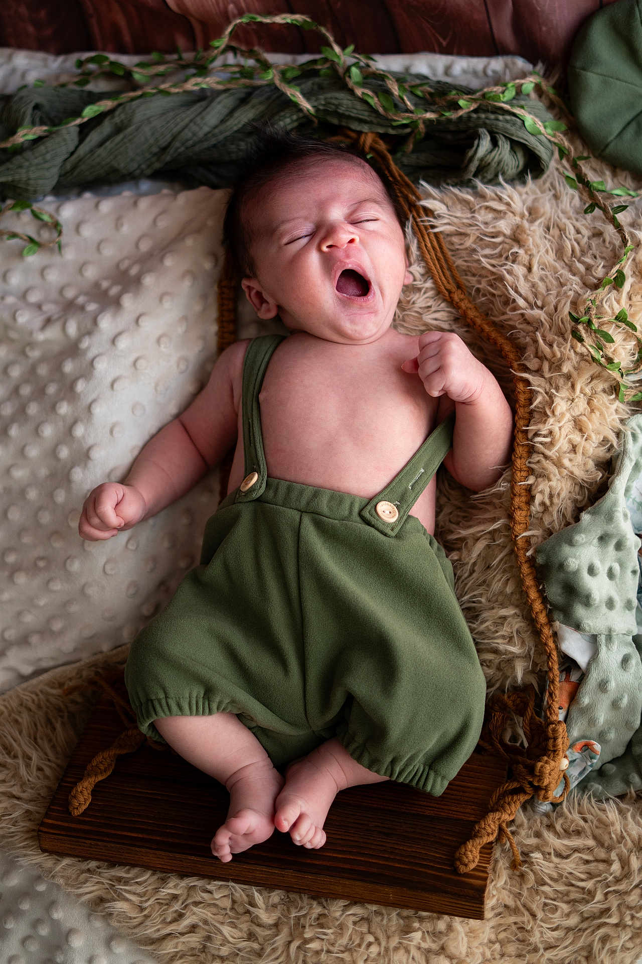 Roméo a rejoint le concours — aidez-le/la à gagner de superbes lots ! baby, infant, yawning, green_overalls, blanket, pillow, soft_texture, cozy, sleepy, cute, newborn, wooden_board, indoors, child, skin, furniture, relaxing, resting, small_person, portrait