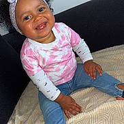 Talya a rejoint le concours — aidez-le/la à gagner de superbes lots ! toddler, child, smiling, headband, curly_hair, pink_shirt, tie_dye, jeans, barefoot, blanket, couch, indoor, happy, cute, portrait, person, seated, baby, fashion, cozy