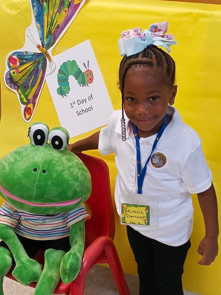 Miracle is registered to the contest to win money with this photo: amphibian, child, child_art, event, facial_expression, frog, fun, green, happy, joy, logo, person, reptile, room, sleeve, smile, stuffed_toy, t_shirt, toad, toddler