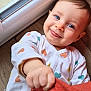 baby, infant, child, blue_eyes, smile, onesie, heart_pattern, hand, floor, window, natural_light, playful, face, cute, indoors, portrait, skin, young_child, happy, clothing