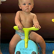 Sébastien participe au concours pour gagner de l'argent avec cette photo : toddler, child, diaper, toy, ride_on, blue, yellow, barefoot, indoor, floor_mat, serious, grip, plastic_toy, person, foot, tattoo, writing, play, young_child, cute