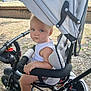Sébastien a rejoint le concours — aidez-le/la à gagner de superbes lots ! toddler, child, stroller, outdoor, blue_eyes, canopy, gravel, hand, foot, white_tank_top, seat, black_frame, sunlight, park, playground, baby, person, summer, daytime, safety_bar