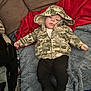 baby, child, hoodie, camouflage, blanket, red_blanket, blue_blanket, boots, pants, clothing, face, person, infant, couch, indoor, floor, cozy, lying_down, casual, cute