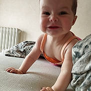 Emy a rejoint le concours — aidez-le/la à gagner de superbes lots ! baby, bed, blanket, child, crawling, cute, expression, face, hand, happy, home, indoor, infant, orange_outfit, person, radiator, room, skin, smile, young_child