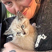 Chandler is registered to the contest to win money with this photo: cat, kitten, person, human, pet, animal, fluffy, cream_fur, blue_eyes, portrait, close_up, cuddling, car, vehicle, tattoo, nose_ring, black_shirt, sunlight, cute, indoors