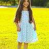 backlighting, child, daylight, fashion, floral_dress, full_body, girl, grass, happy, long_hair, meadow, nature, necklace, outdoor, park, photography, portrait, smiling, standing, sunlight