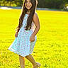 Maria Alice is registered to the contest to win money with this photo: child, girl, smiling, outdoor, portrait, garden, meadow, grass, sunlight, backlighting, floral_dress, long_hair, necklace, shoes, standing, walking, happy, nature, park, photography